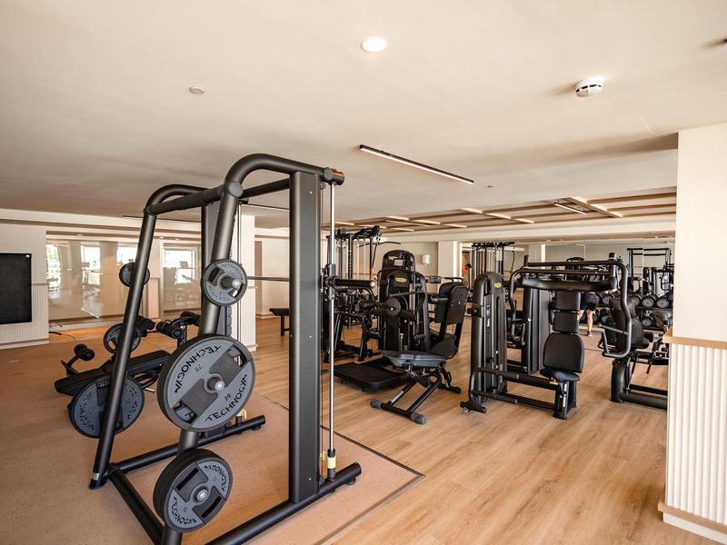 Attrezzature fitness moderne in una palestra luminosa con pavimenti in legno e grandi specchi.