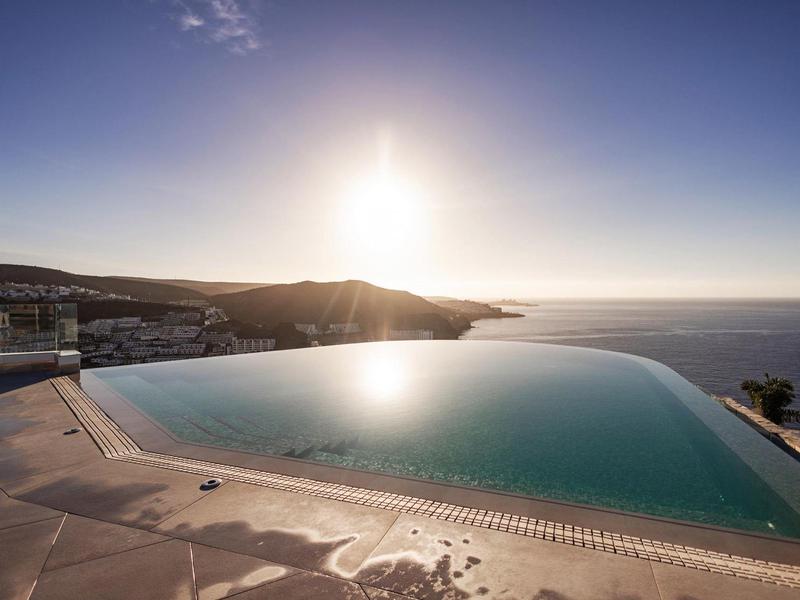 Piscina a sfioro con vista mare al tramonto in un hotel.