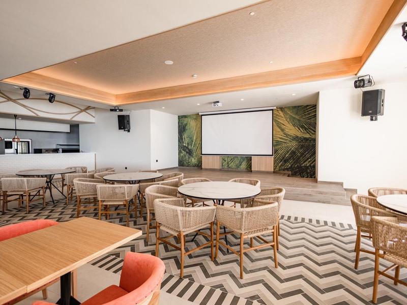 Sala eventi moderna con area salotto, bar e grande schermo di proiezione.