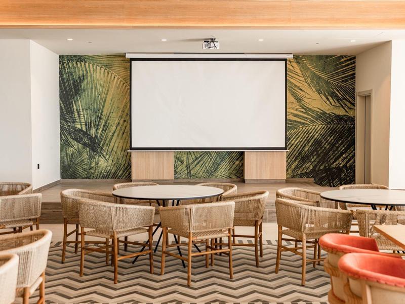 Sala conferenze moderna con tavoli rotondi, sedie in vimini e grande schermo davanti a parete decorativa