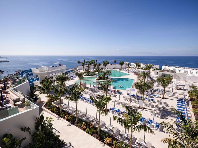 Vista di un hotel con più piscine, lettini e edifici bianchi vicino al mare.