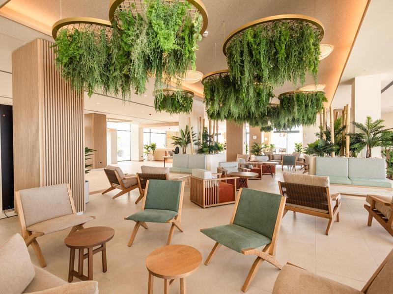 Lounge di hotel moderna e luminosa con piante verdi, poltrone comode e vegetazione sospesa al soffitto.