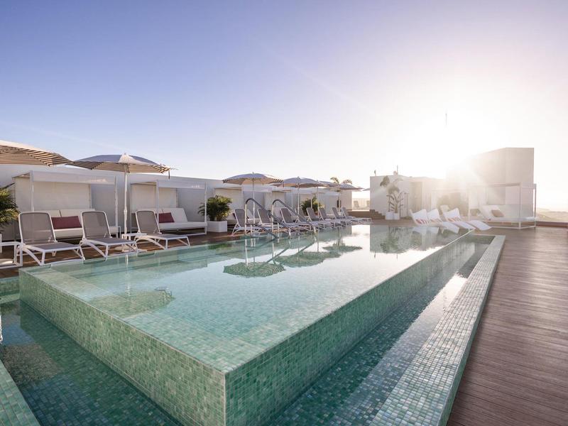 Piscina esterna moderna con lettini e ombrelloni sul tetto dell'hotel al tramonto.