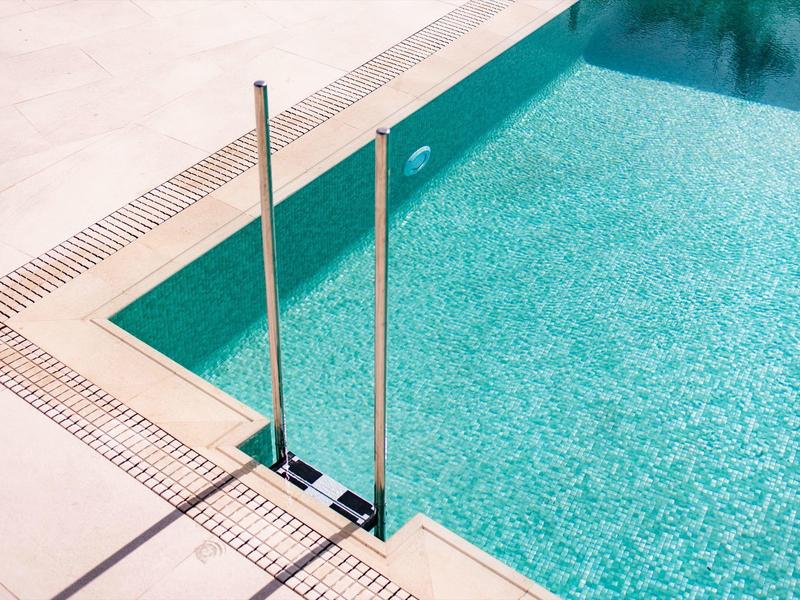 Vista di una piscina con acqua limpida, una scala in acciaio inossidabile e un bordo beige.