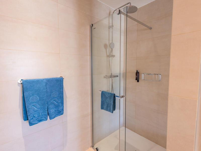 Area doccia moderna con porta in vetro, doccia a pioggia e asciugamano blu in bagno.