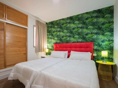 Modernes Schlafzimmer mit grünem Pflanzenmuster an der Wand, rotem Kopfteil und weißen Betten.