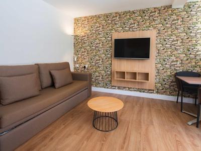 Gemütliches Wohnzimmer mit braunem Sofa, runder Holztisch, Steinwand und Flachbildfernseher.