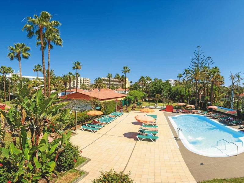 Buitenzwembad omgeven door palmbomen en ligbedden met rood dak op de achtergrond.