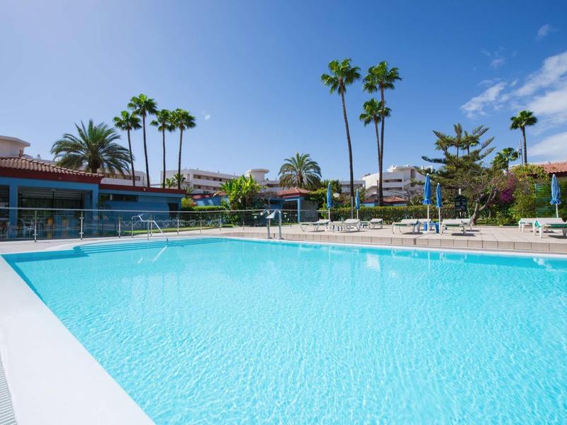 Buitenzwembad met helder water omringd door palmbomen en appartementen.