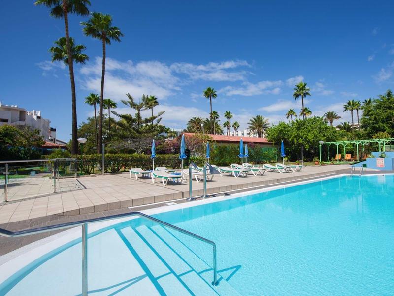 Buitenzwembad met ligstoelen en palmbomen onder een heldere hemel bij een resort.