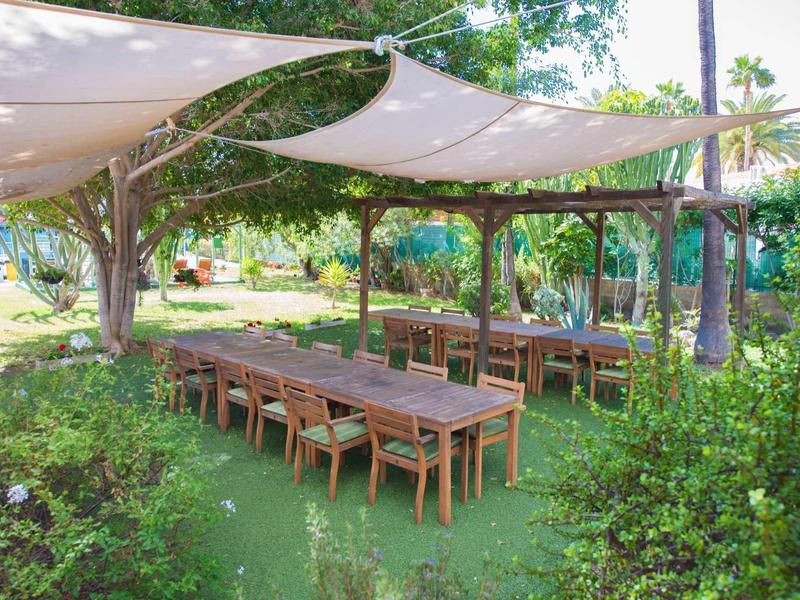 Buitenterras met houten tafels en stoelen onder zonneschermen in een tuin.