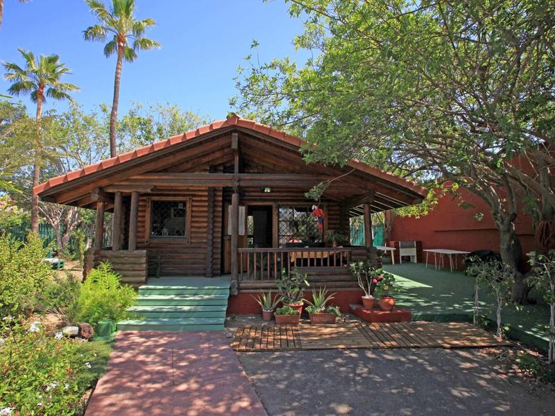 Rustieke houten hut met veranda omgeven door groen onder een heldere hemel.