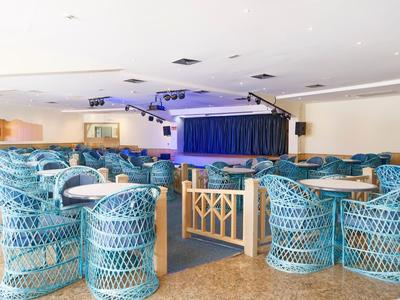 Duża sala konferencyjna z niebieskimi wiklinowymi krzesłami i sceną z niebieskimi zasłonami.