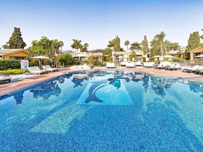 Grande piscine extérieure avec eau bleue et chaises longues dans une station ensoleillée.