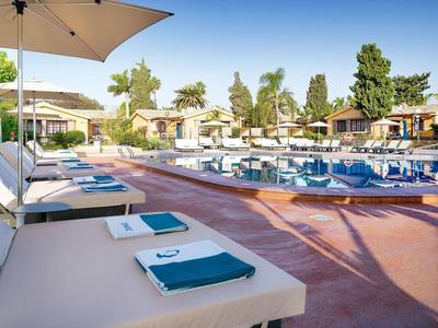 Słoneczny basen z białymi leżakami i niebieskimi ręcznikami w ogrodzie hotelowym.