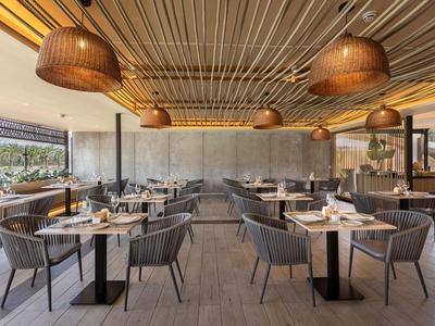 Restaurante moderno de hotel con muebles de madera, lámparas colgantes y grandes ventanas con vista al verde.