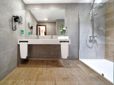 Baño moderno con ducha grande, espejo y dos toallas en el lavabo.