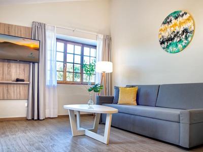 Salon moderne avec canapé gris, table ronde et art mural près de la fenêtre et téléviseur.