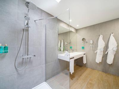 Salle de bain d'hôtel moderne avec douche en verre, lavabo blanc et deux peignoirs accrochés au mur.
