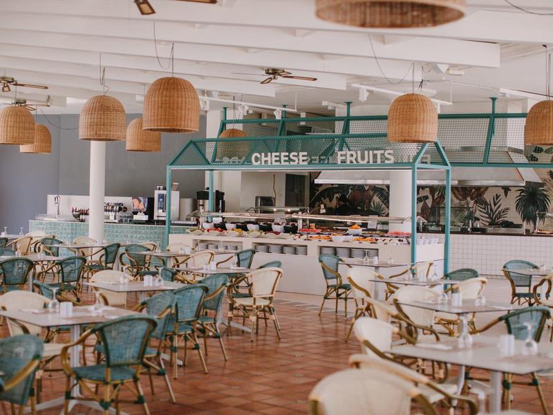 Restaurant lumineux avec des chaises vertes et des lampes suspendues au comptoir fromage et jambon.