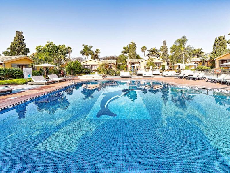 Grande piscine extérieure avec eau bleue et chaises longues dans une station ensoleillée.