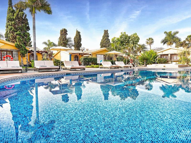 Grande piscine avec transats et palmiers dans un complexe hôtelier.