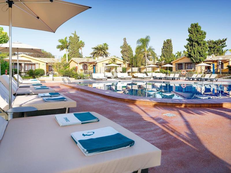 Espace piscine avec transats, serviettes bleues et parasols dans un complexe hôtelier ensoleillé.