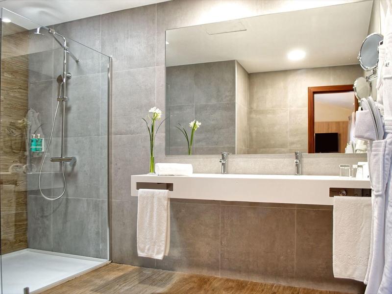 Salle de bain d'hôtel moderne avec douche en verre, grand miroir et lavabo blanc.