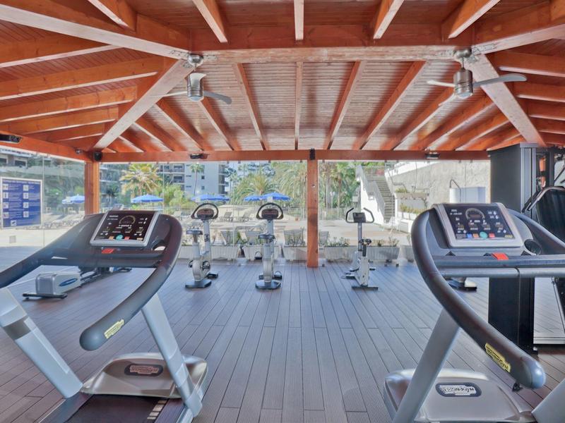 Área de gimnasio con cintas de correr y bicicletas estáticas bajo techo de madera con vista a exteriores.