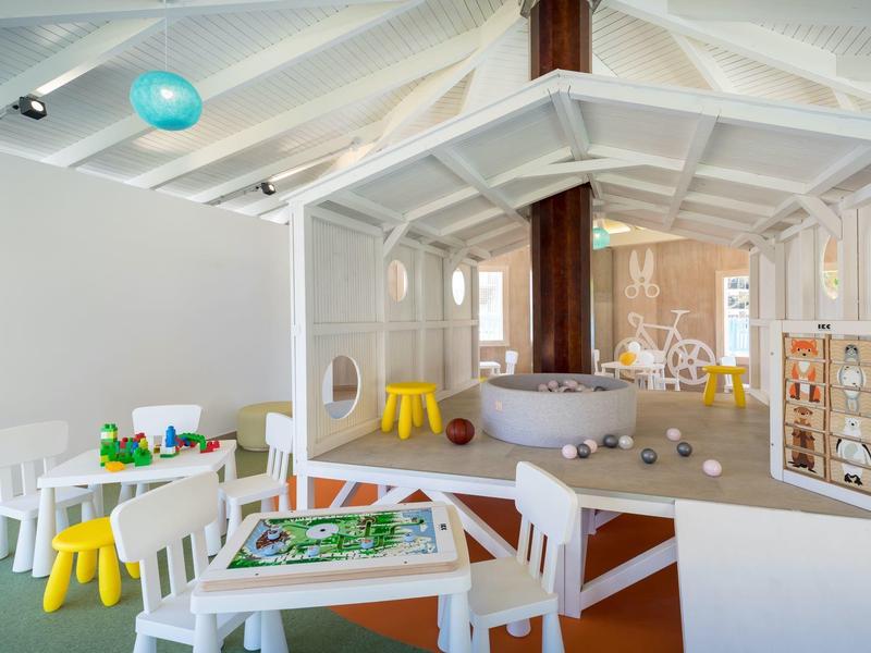 Área de juegos infantiles con mesas blancas, sillas de colores y un marco de casa en el hotel.