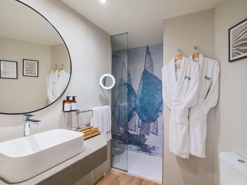 Baño moderno con lavabo, espejo redondo y ducha con pared de vidrio decorado.