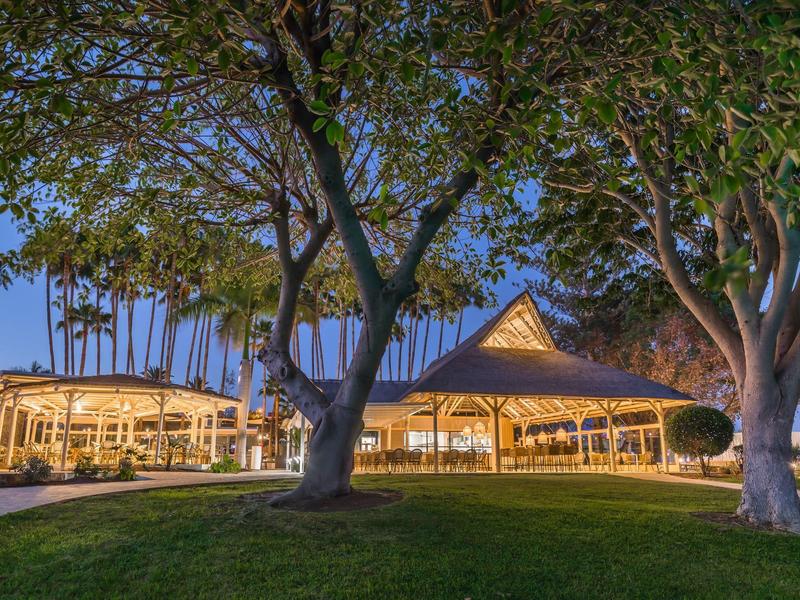 Edificio de hotel iluminado al atardecer con árboles y césped cuidado en primer plano.