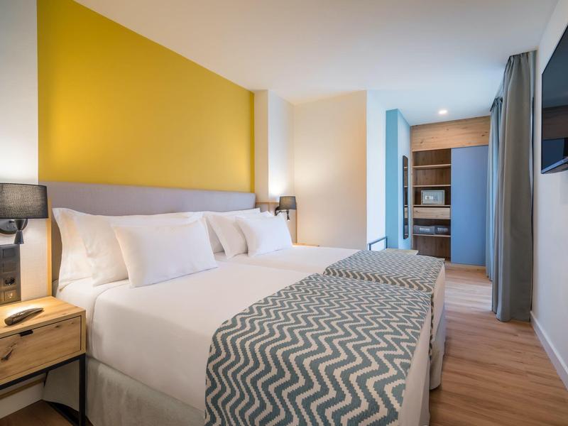 Habitación de hotel moderna con cama grande, pared amarilla y suelo de madera.