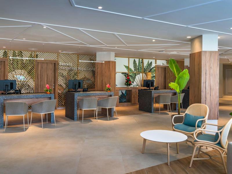 Área de recepción moderna en hotel con zonas de trabajo, sillas y plantas verdes con luz cálida