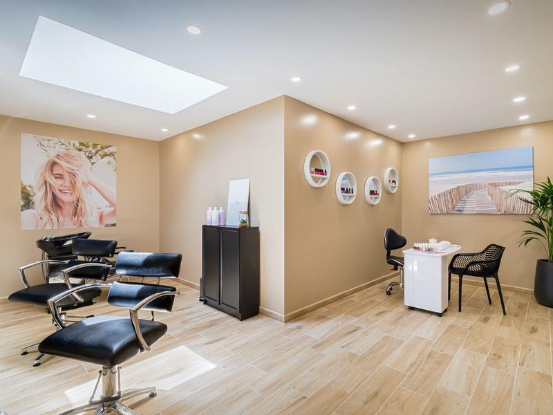 Salón de peluquería luminoso con mobiliario moderno, suelo de madera, sillas cómodas y grandes cuadros en la pared.