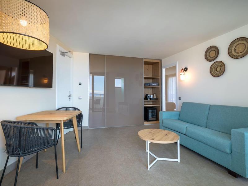 Sala de estar moderna con sofá, mesa, silla y TV de pared en un alojamiento hotelero.