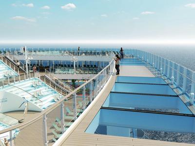 Vista di una terrazza piscina di un hotel con ringhiera in vetro e oceano sullo sfondo sotto un cielo limpido.