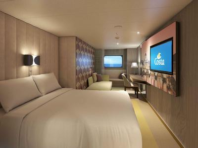 Camera d'hotel moderna con letto grande, TV e area salotto in tonalità calde.