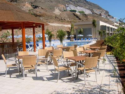 Hotel outdoor area with wooden tables and chairs beside a pool and mountains in the background.
