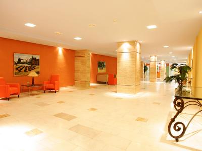 Bright hotel corridor with beige marble tile, orange chairs, and columns.