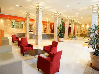 Bright hotel lobby with red armchairs, white columns, and modern lighting.