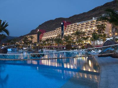 Large hillside hotel with illuminated outdoor pool at dusk.