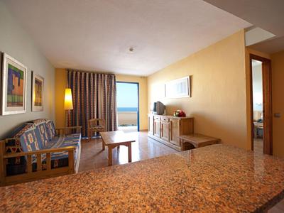 Cozy hotel room with sofa, TV, table, and balcony overlooking the sea.