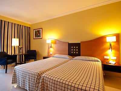 Hotel room with two single beds, yellow walls, and a table with two chairs.