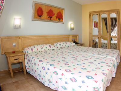 Brightly furnished hotel room with double bed, wooden furniture, and small nightstand.
