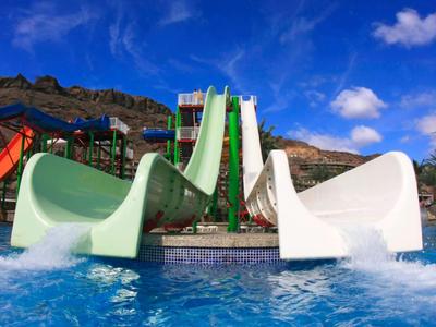 Water park with colorful slides against a blue sky with clouds and mountains, perfect for vacation.