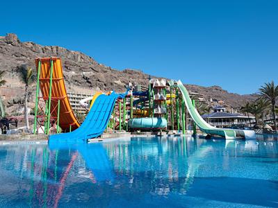 Colorful water slides over a clear blue pool with rocky landscape and blue sky in the background.
