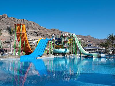Barevný aquapark u hotelového bazénu s skalnatou horou a modrou oblohou.