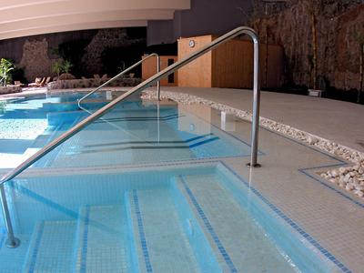 Modern indoor pool with wide steps and stainless steel handrail, surrounded by light flooring.