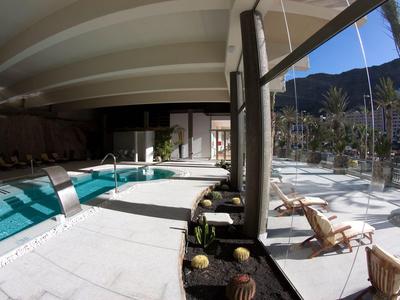 Modern indoor pool area with white floors and large window overlooking mountains.